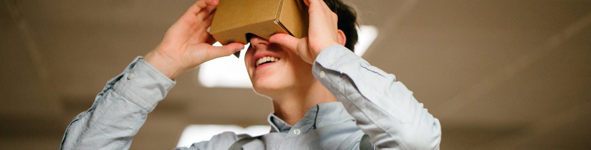 man in grey dress shirt using brown cardboard vr glasses